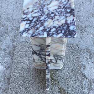 May include: A square pedestal stand crafted from polished marble featuring a distinct veined pattern in shades of white, cream, and deep purple. The structure consists of a flat top surface supported by a central vertical column base.