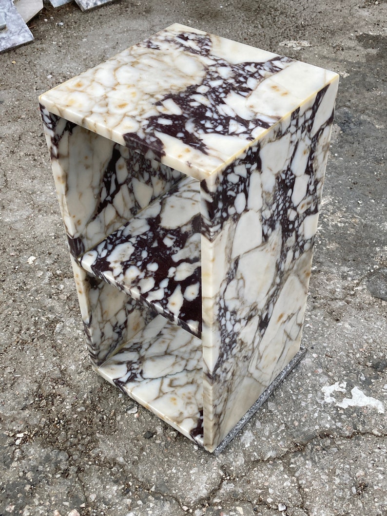 May include: A white and brown marble end table with two shelves. The table has a square top and a rectangular base.