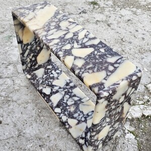 May include: A rectangular marble shelf with a unique open design. The shelf features a cream, black, and gray speckled pattern. The shelf is made of stone and is suitable for displaying decorative items.