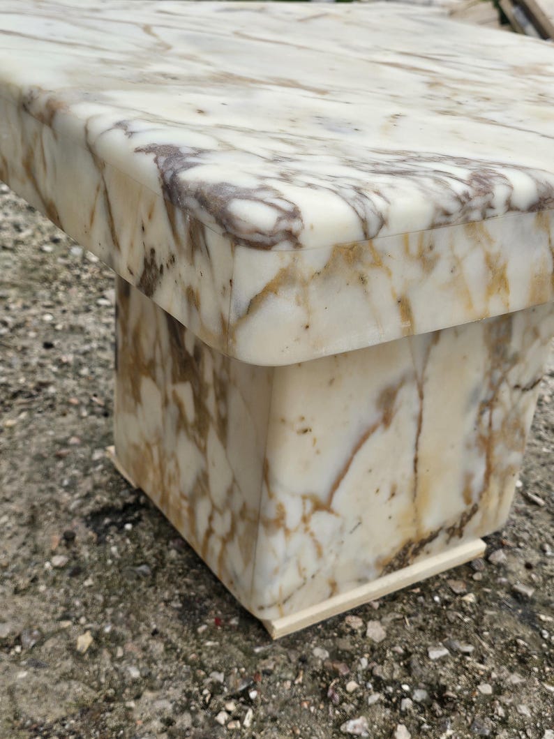 May include: A square side table constructed from polished white marble with prominent brown and grey veining throughout. The table features a thick, overhanging top surface supported by a solid, block-style pedestal base with smooth, rounded edges.
