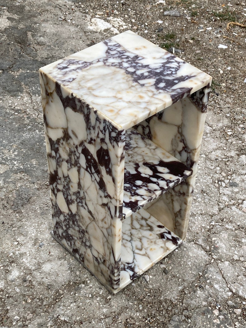May include: A white and purple marble end table with two shelves. The table has a square top and a rectangular base.
