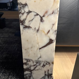 May include: Close-up of a white marble slab with brown and pink veining. The marble has a polished finish and is smooth to the touch.