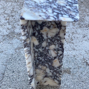 May include: A C-shaped side table constructed from a single piece of polished stone featuring a complex, mottled pattern of white, cream, and dark purple-grey veins. The structure has a flat rectangular top and a vertical support panel.