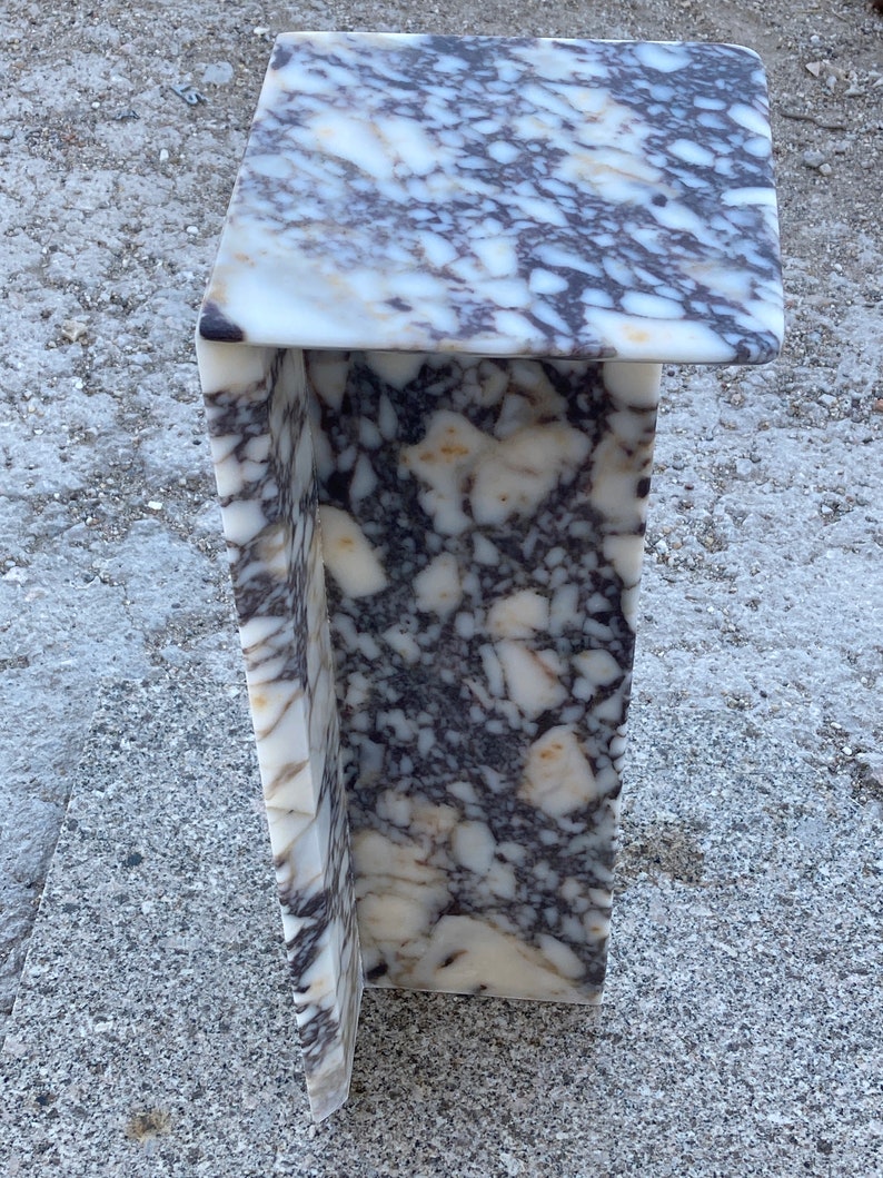 May include: A C-shaped side table constructed from a single piece of polished stone featuring a complex, mottled pattern of white, cream, and dark purple-grey veins. The structure has a flat rectangular top and a vertical support panel.