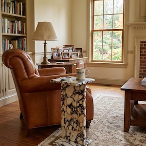 May include: A tall, rectangular side table crafted from white and black marbled stone with a smooth, polished finish. The table features a flat top surface and a sturdy base, positioned in a room with a leather armchair and a ceramic mug.