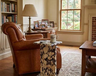 May include: A tall, rectangular side table crafted from white and black marbled stone with a smooth, polished finish. The table features a flat top surface and a sturdy base, positioned in a room with a leather armchair and a ceramic mug.