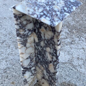 May include: A tall, L-shaped pedestal stand crafted from polished stone with a distinct brecciated pattern. The surface features a complex mix of white, cream, and deep purple-brown angular fragments embedded in a smooth, glossy finish.