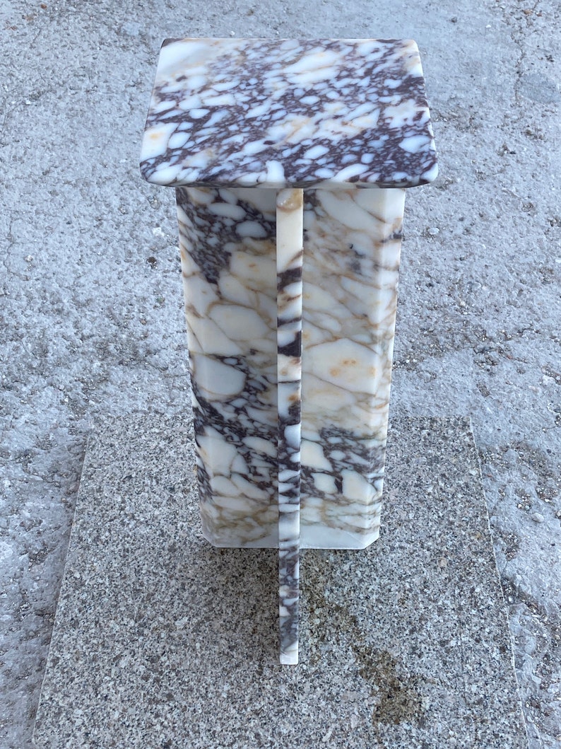 May include: A tall, rectangular pedestal stand crafted from white marble with prominent dark purple and brown veining. The structure features a flat square top surface supported by a central vertical column with a cross-shaped base design.