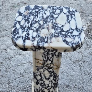 K&ouml;nnte beinhalten: Ein Marmor-Sockeltisch mit rechteckiger Platte und quadratischem Sockel. Der Tisch weist ein auff&auml;lliges Muster aus schwarzen und wei&szlig;en Adern im gesamten Stein auf. Der Sockel ist etwa 76 cm hoch.