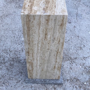 Puede incluir: Un pedestal cuadrado de piedra travertina de color marr&oacute;n claro con una base gris oscuro. El pedestal est&aacute; hecho de piedra natural con un patr&oacute;n veteado &uacute;nico.