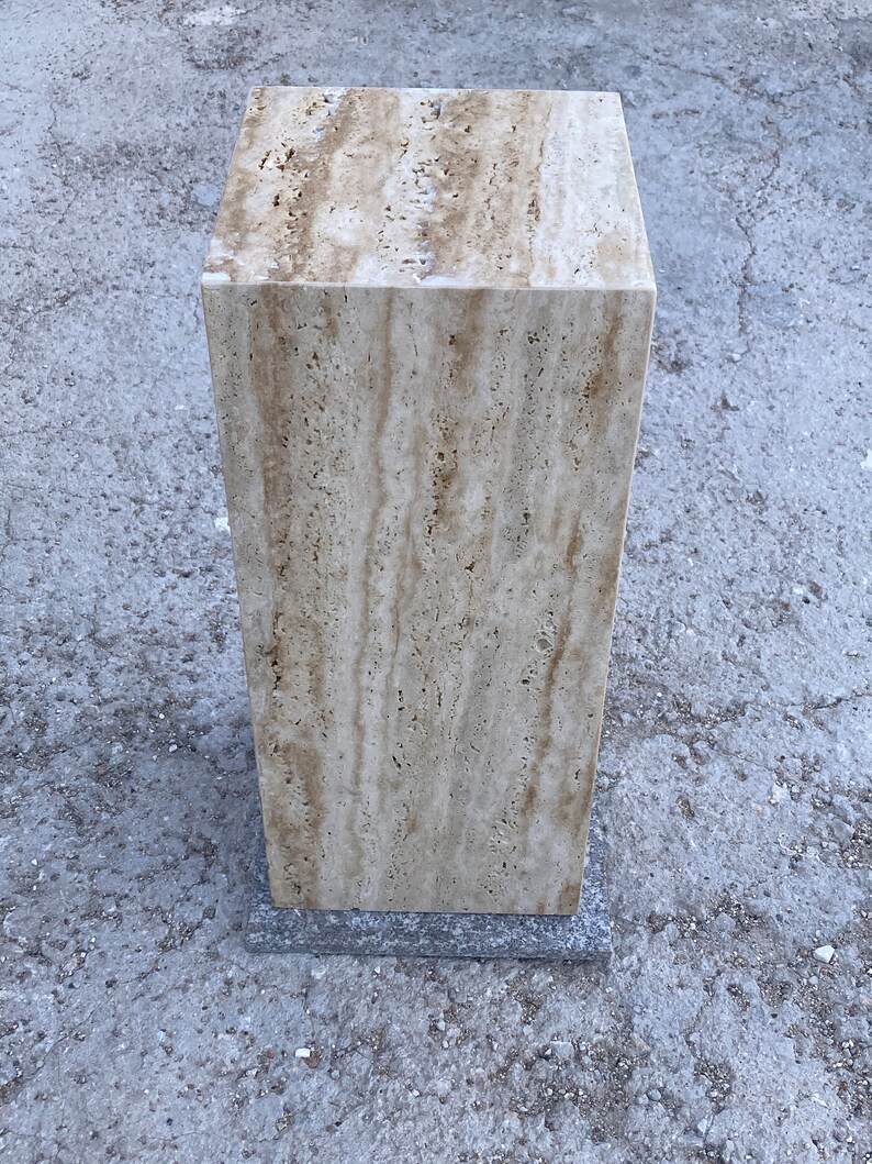 Puede incluir: Un pedestal cuadrado de piedra travertina de color marr&oacute;n claro con una base gris oscuro. El pedestal est&aacute; hecho de piedra natural con un patr&oacute;n veteado &uacute;nico.