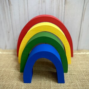 May include: A wooden rainbow arch made of four stacked arches in red, yellow, green, and blue.