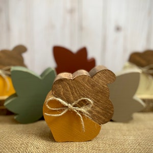 May include: Five wooden acorn ornaments with a rustic brown finish. Each acorn is decorated with a simple twine bow and painted in a variety of fall colors, including yellow, green, and brown.