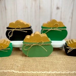 May include: Four wooden pot of gold decorations. The pots are painted green and black with gold coins on top. They are tied with gold twine.