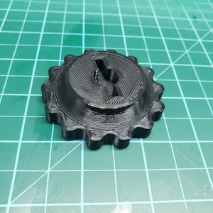May include: A black plastic gear with a central hole and a series of teeth around the edge.