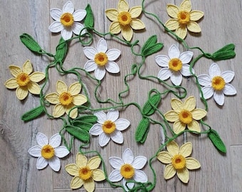 May include: A garland of crocheted daffodils with white and yellow flowers and green leaves.