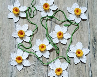 May include: A garland of crocheted white daffodils with yellow centers. The garland is strung together with green yarn and is perfect for spring decor.