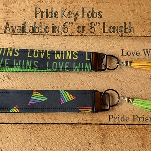 May include: Two Pride key fobs with black straps. One reads "LOVE WINS" in green and yellow, the other features rainbow prism designs. Both have metal hardware and tassel accents. Available in 6" or 8" lengths.