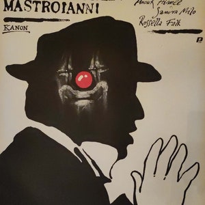 May include: A black and white poster for the film 8 1/2, directed by Federico Fellini and starring Marcello Mastroianni. The poster features a silhouette of a man in a suit and hat, with a red clown nose. The text on the poster reads "8 1/2", "Federico Fellini", "Marcello Mastroianni", "Claudia Cardinale", "Anouk Aimee", "Sandra Milo", "Rossella Falk", and "Kanon".