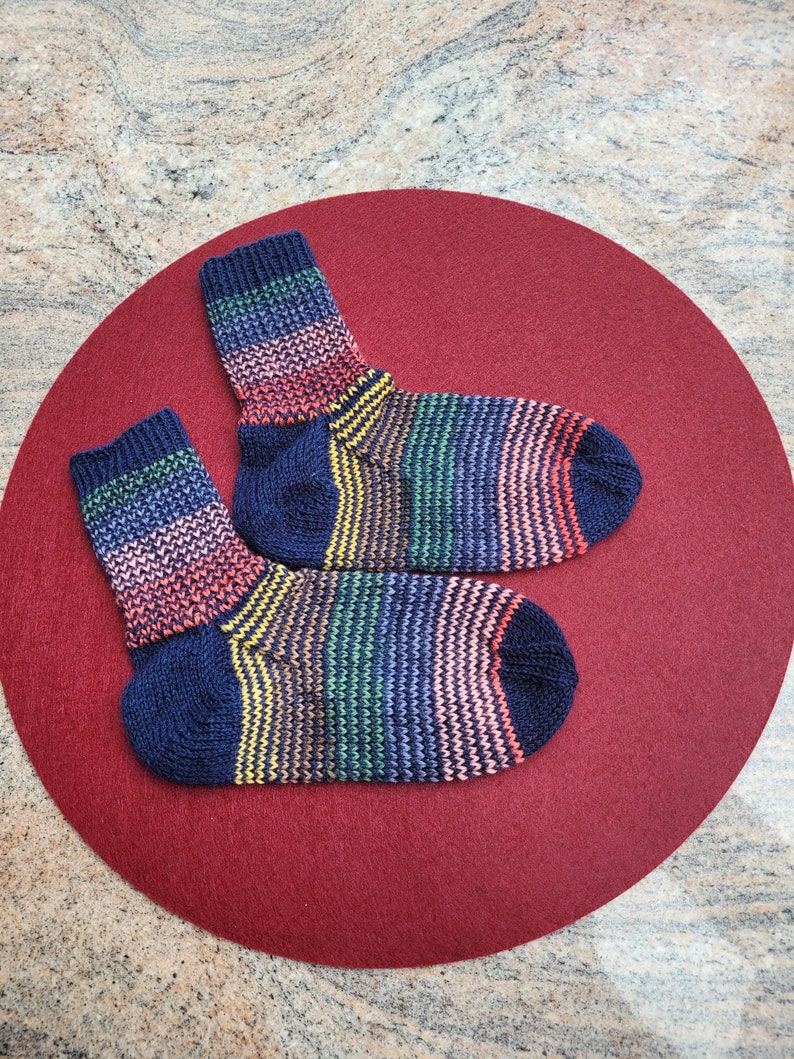 May include: Two colorful striped socks with a navy blue base color. The socks are on a red background.