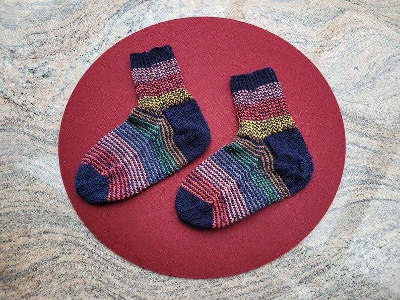 May include: Two colorful striped socks with a dark blue background. The socks are on a red background.