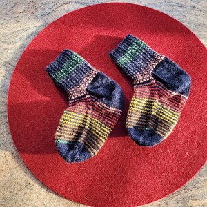 May include: Two colorful striped socks with a dark blue base color. The socks are on a red circular surface.