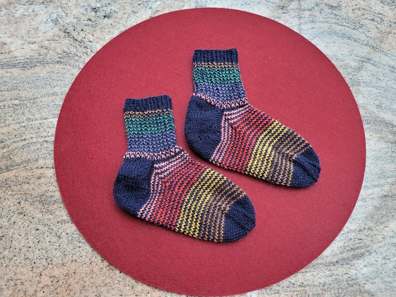 May include: Two pairs of colorful striped socks with a dark blue base color. The socks are on a red background.