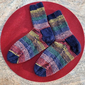 May include: Two colorful striped socks with a dark blue background. The socks are made of a soft, knitted fabric and have a rainbow pattern.