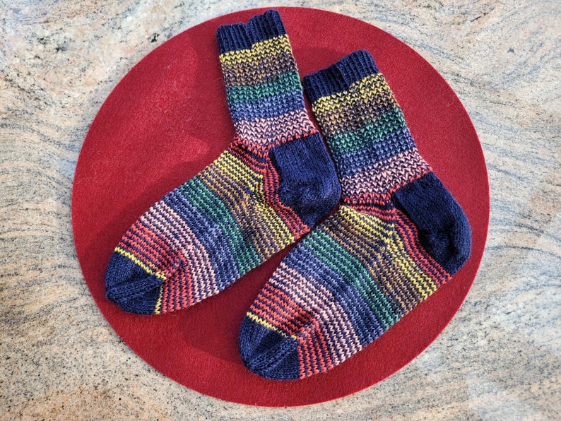 May include: Two colorful striped socks with a dark blue background. The socks are made of a soft, knitted fabric and have a rainbow pattern.