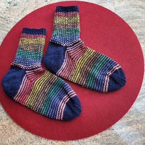 May include: Two pairs of colorful striped socks with a dark blue base color. The socks are laid out on a red felt surface.