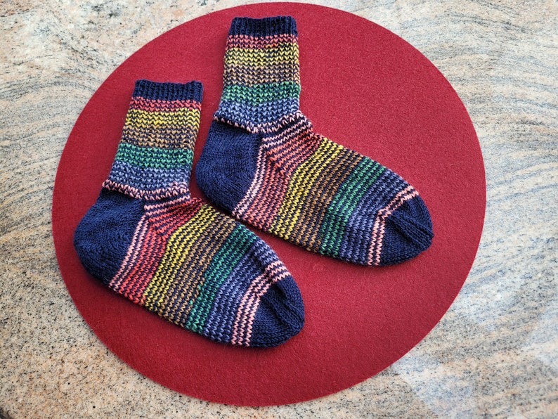 May include: Two pairs of colorful striped socks with a dark blue base color. The socks are laid out on a red felt surface.