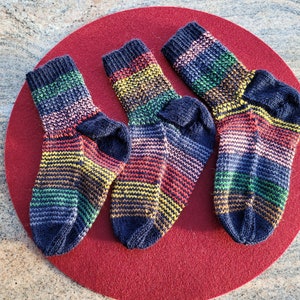 May include: Three pairs of colorful striped socks with a dark blue base color. The socks are arranged on a red circular surface.