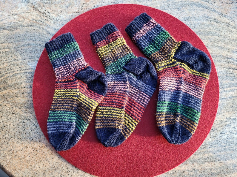 May include: Three pairs of colorful striped socks with a dark blue base color. The socks are arranged on a red circular surface.