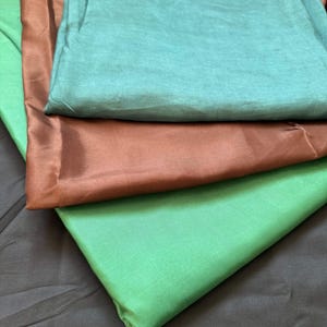Peut inclure: Quatre échantillons de tissu de différentes couleurs : sarcelle, marron, vert et noir. Les échantillons sont pliés et superposés.