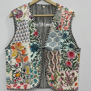 Könnte beinhalten: Eine weiße gesteppte Weste mit einem schwarz-weiß gestreiften Futter. Die Weste besteht aus Patchwork-Stoff mit floralen und geometrischen Mustern in den Farben Rosa, Blau, Grün und Gelb. Die Weste hat einen V-Ausschnitt und einen Bindeverschluss.