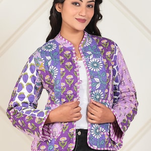 Könnte beinhalten: Gesteppte Jacke mit einem lebendigen Blumen- und Fruchtmuster in Lila, Weiß und Grün. Die Jacke hat einen Stehkragen und einen Knopfverschluss. Der Text "CraftHaveli" ist sichtbar.