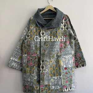 Puede incluir: Una chaqueta azul claro con un estampado floral en amarillo, rosa y verde oscuro con costuras blancas visibles. La prenda tiene un cuello ancho y doblado de tela gris oscuro liso y el texto CraftHaveli impreso en la parte central.