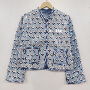 May include: A light blue quilted jacket with a floral print and a white and blue striped collar. The jacket has two pockets and a button closure. The text "CraftHaveli" is printed on the front of the jacket.