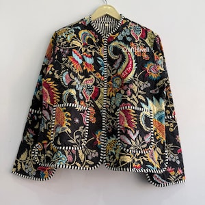 May include: A quilted jacket featuring a black base with a vibrant, multi-coloured floral and paisley print. The garment includes two front pockets, a round neckline, and black and white striped trim along the edges. The text CraftHaveli is visible.