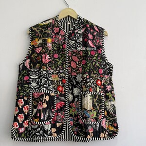 May include: A sleeveless quilted vest featuring a black base with a vibrant floral pattern in shades of red, pink, yellow, and white. The garment has two front patch pockets and is finished with black and white striped trim along the edges.
