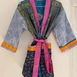 Könnte beinhalten: Ein Patchwork-Kimono-Mantel mit einer Mischung aus Mustern und Farben. Der Mantel hat ein türkis-, grau- und blaues Blumenmuster mit einem leuchtend rosa Besatz und Gürtel. Die Ärmel haben ein hellblaues Blumenmuster mit orangefarbenem Besatz.