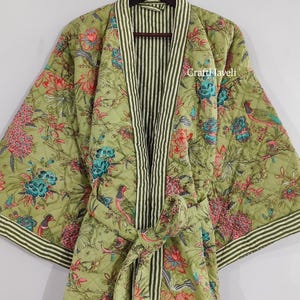 Puede incluir: Bata verde acolchada con un estampado floral y de pájaros. La bata tiene un ribete a rayas y un cinturón a juego. El texto "CraftHaveli" es visible en el lado derecho de la bata.