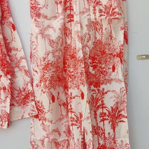 May include: White pajama pants with a red and white print of palm trees and birds. The pants have a drawstring waist.