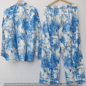 May include: A white pajama set with a blue and white palm tree and bird print. The set includes a long-sleeved shirt and pants.