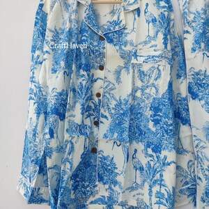 May include: A white pajama top with a blue and white floral print featuring birds and palm trees. The top has a button-up front and a collar.