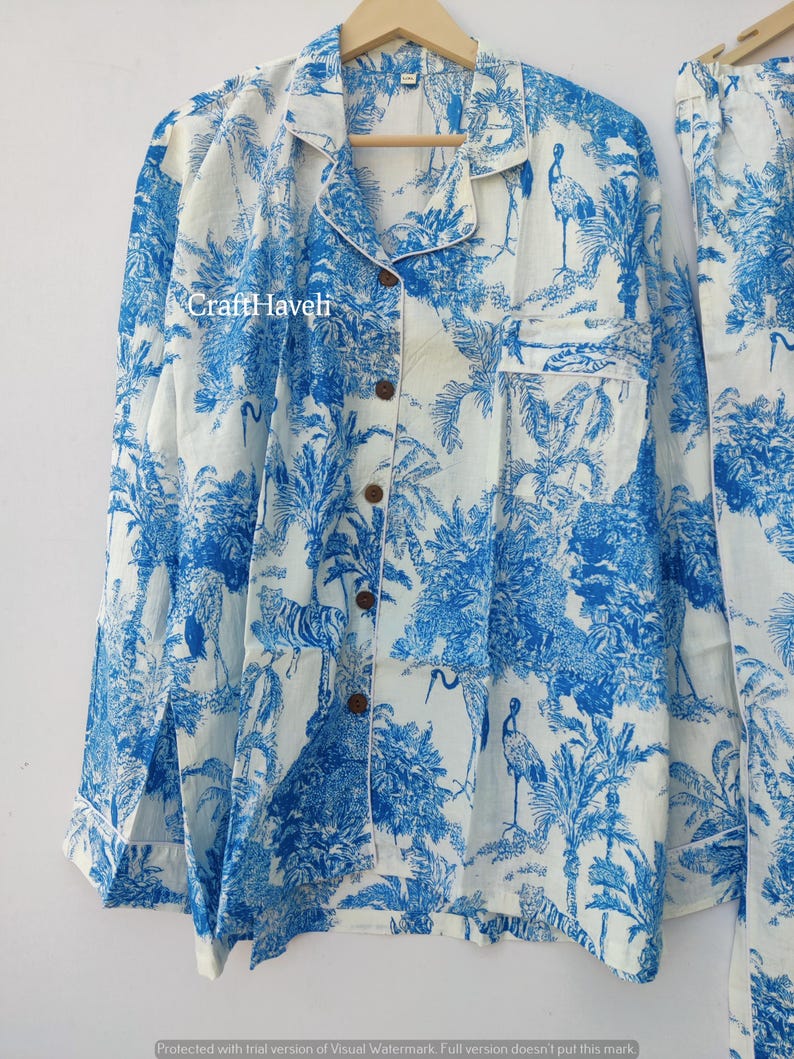 May include: A white pajama top with a blue and white floral print featuring birds and palm trees. The top has a button-up front and a collar.