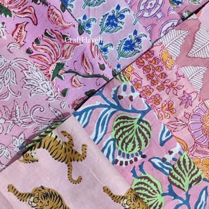 Op de afbeelding: Een verzameling roze stofstalen met verschillende bloemen- en dierenprints. De prints omvatten tijgers, bladeren en bloemen. De stof is lichtroze met blauwe, groene en gele accenten.