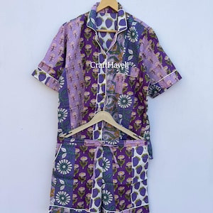 Peut inclure: Ensemble de pyjama à imprimé floral violet et blanc, comprenant une chemise boutonnée à manches courtes et un short assorti. L'ensemble présente divers motifs floraux et le texte "CraftHaveli". Les bords sont bordés d'un passepoil blanc.