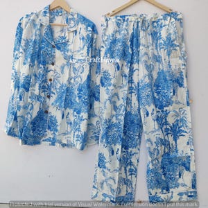 May include: A white pajama set with a blue and white tropical print featuring palm trees and birds. The set includes a long-sleeved shirt with a button-up front and matching pants.