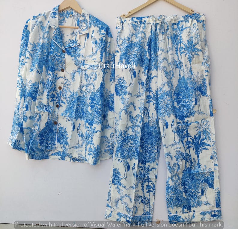 May include: A white pajama set with a blue and white tropical print featuring palm trees and birds. The set includes a long-sleeved shirt with a button-up front and matching pants.
